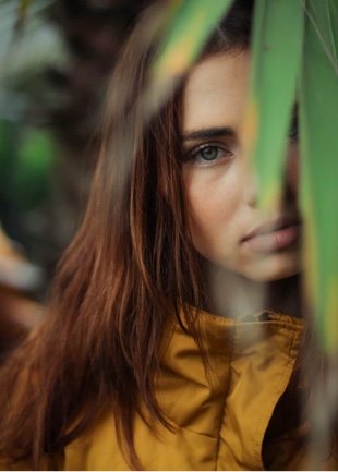 A portrait of a woman with her face partially covered by a leaf