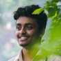 A portrait of a man smiling while looking on the side near some leaves