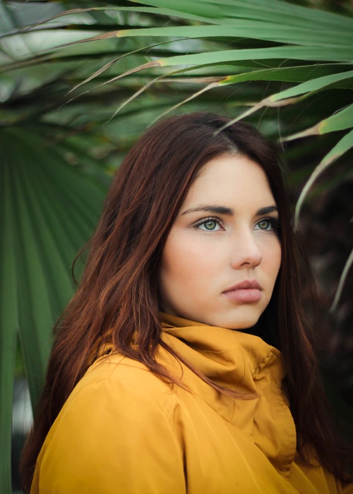 A portrait photo of a woman with dark brown hair wearing a yellow jacket under a tree