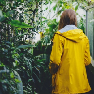 A woman wearing a yellow rainjacket surrounded by plants and trees